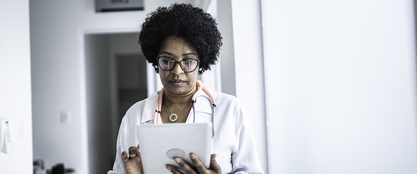 A doctor wearing a stethoscope looks at a tablet device while standing in a brightly lit hallway of a corporate law office.