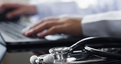A person types on a laptop with a stethoscope resting on the desk in the foreground, highlighting the intersection of healthcare and intellectual property law.
