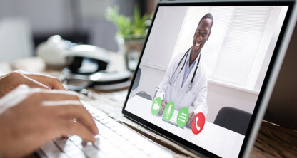 A person types on a laptop while participating in a video call with a doctor, similar to how chicago lawyers connect with clients remotely from a corporate law office.