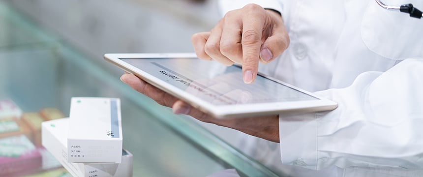 A person in a white lab coat uses a tablet at a counter with medicine boxes nearby, as if preparing documents for an intellectual property law case.