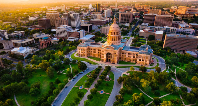 Aerial view of the Texas State Capitol building surrounded by green lawns and city buildings in downtown Austin, Texas, reminiscent of the impressive settings near a top corporate law office or litigation support firm.