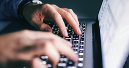 Close-up of hands typing on a laptop keyboard in a corporate law office, with the screen partially visible and the background blurred.