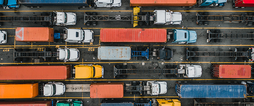 Aerial view of multiple trucks with colorful shipping containers lined up in parallel lanes at a transport facility near a corporate law office offering litigation support.