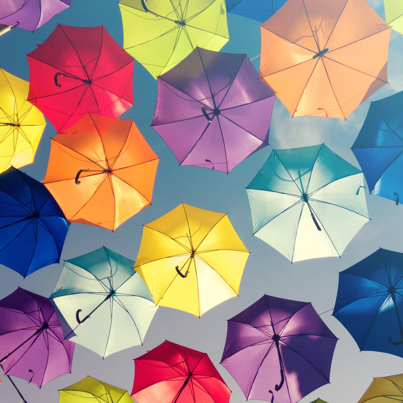 Colorful umbrellas are suspended in the air against a blue sky, viewed from below—a vibrant scene in the city often frequented by Chicago lawyers. The umbrellas are open and arranged in a scattered pattern.