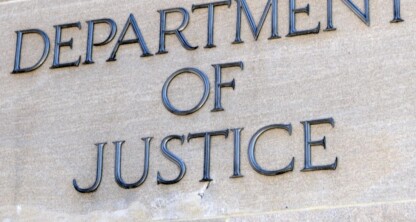 A stone wall with the words "Department of Justice" engraved in large capital letters, evoking the authority of major law offices or a hub for intellectual property law.