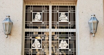 Entrance doors of the Federal Trade Commission building, featuring decorative metalwork with ship and airplane designs, flanked by two wall-mounted lanterns—an inspiring sight for any corporate law office or chicago lawyers seeking justice.