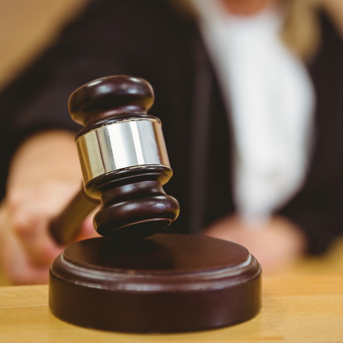 A judge's hand holding a wooden gavel about to strike a sounding block in a courtroom, symbolizing the critical role of litigation support in cases involving intellectual property law.