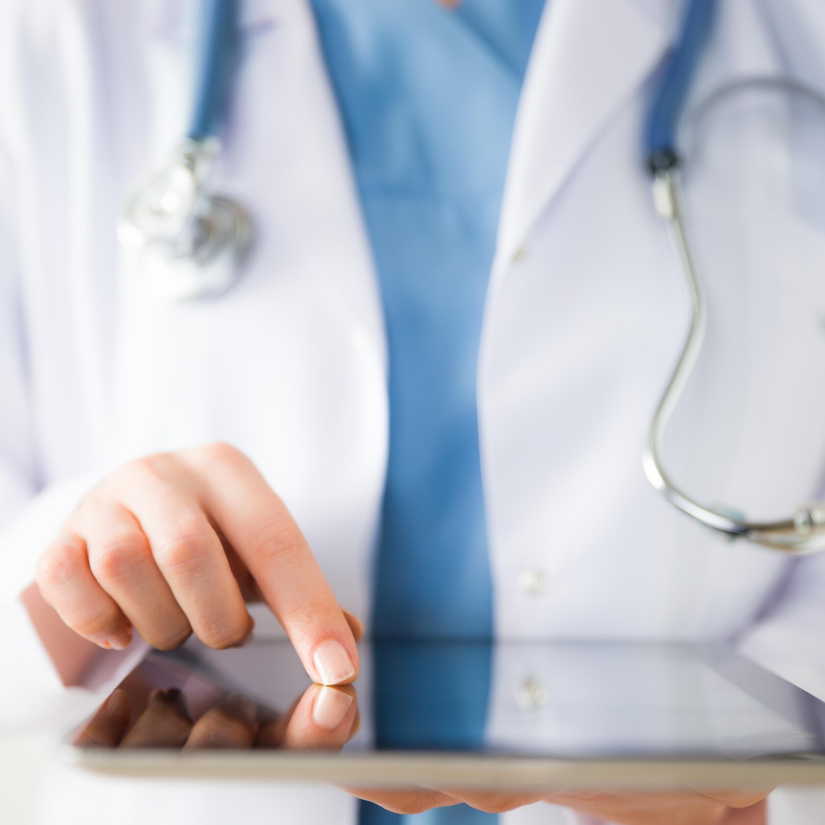 A doctor wearing a white coat and stethoscope uses a tablet, much like lawyers in Chicago rely on technology for efficient litigation support—touching the screen with one finger to access vital information.