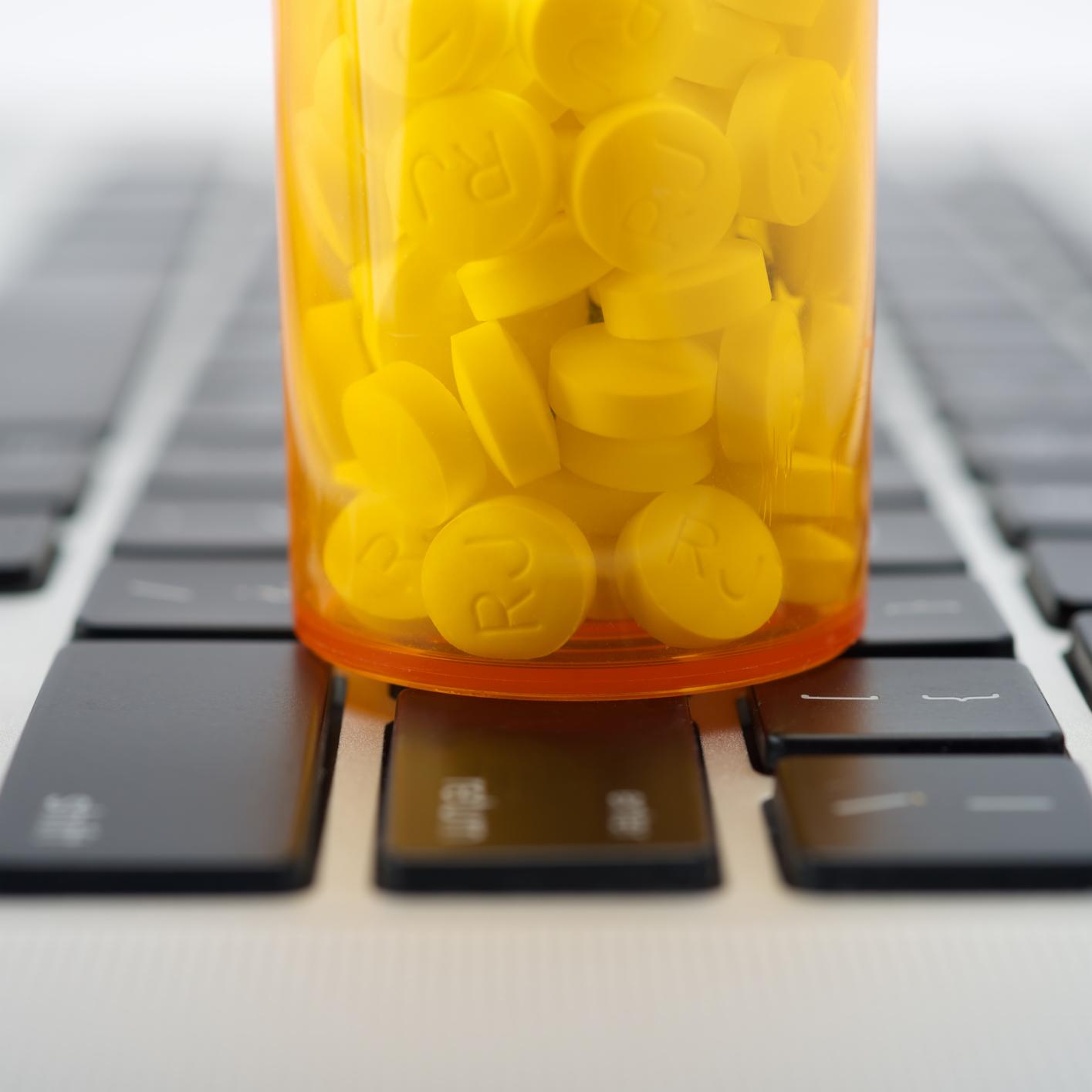A prescription pill bottle filled with yellow tablets sits on top of a computer keyboard in a corporate law office.