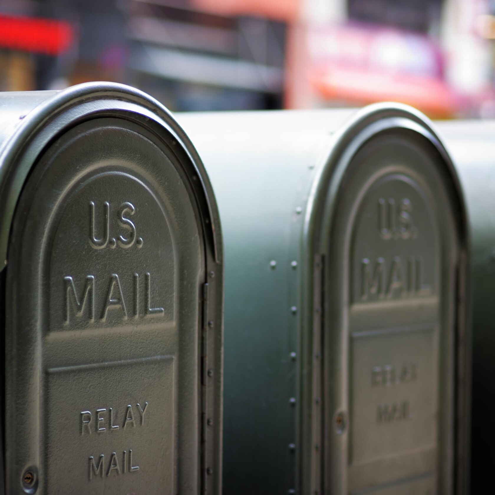 Close-up of two green U.S. Mail relay mailboxes with embossed lettering, positioned side by side on a city street near a busy corporate law office of experienced lawyers in Chicago.