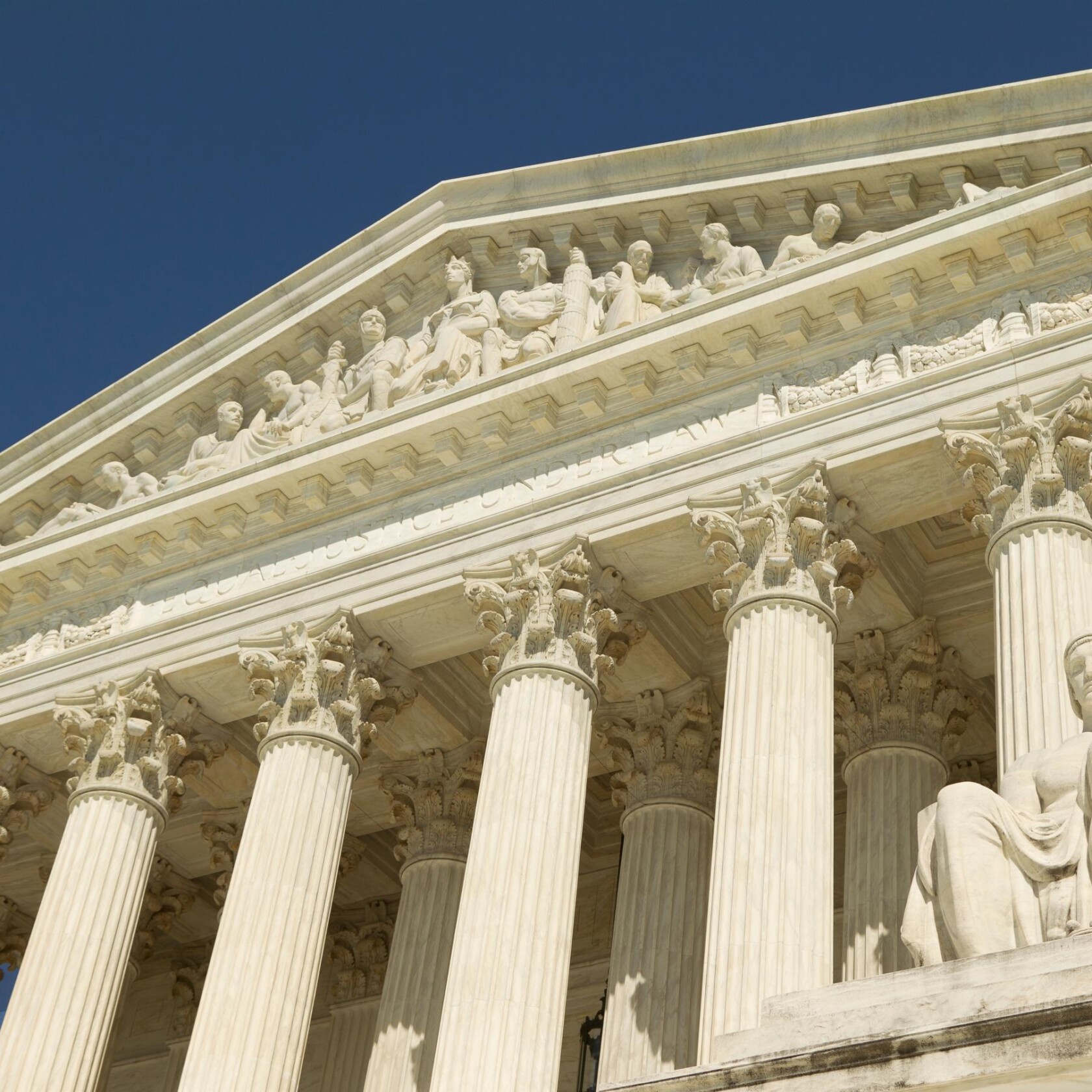 The facade of a neoclassical building with tall columns and sculpted figures, viewed from below against a clear blue sky, evokes the prestige of Chicago lawyers and distinguished law offices.