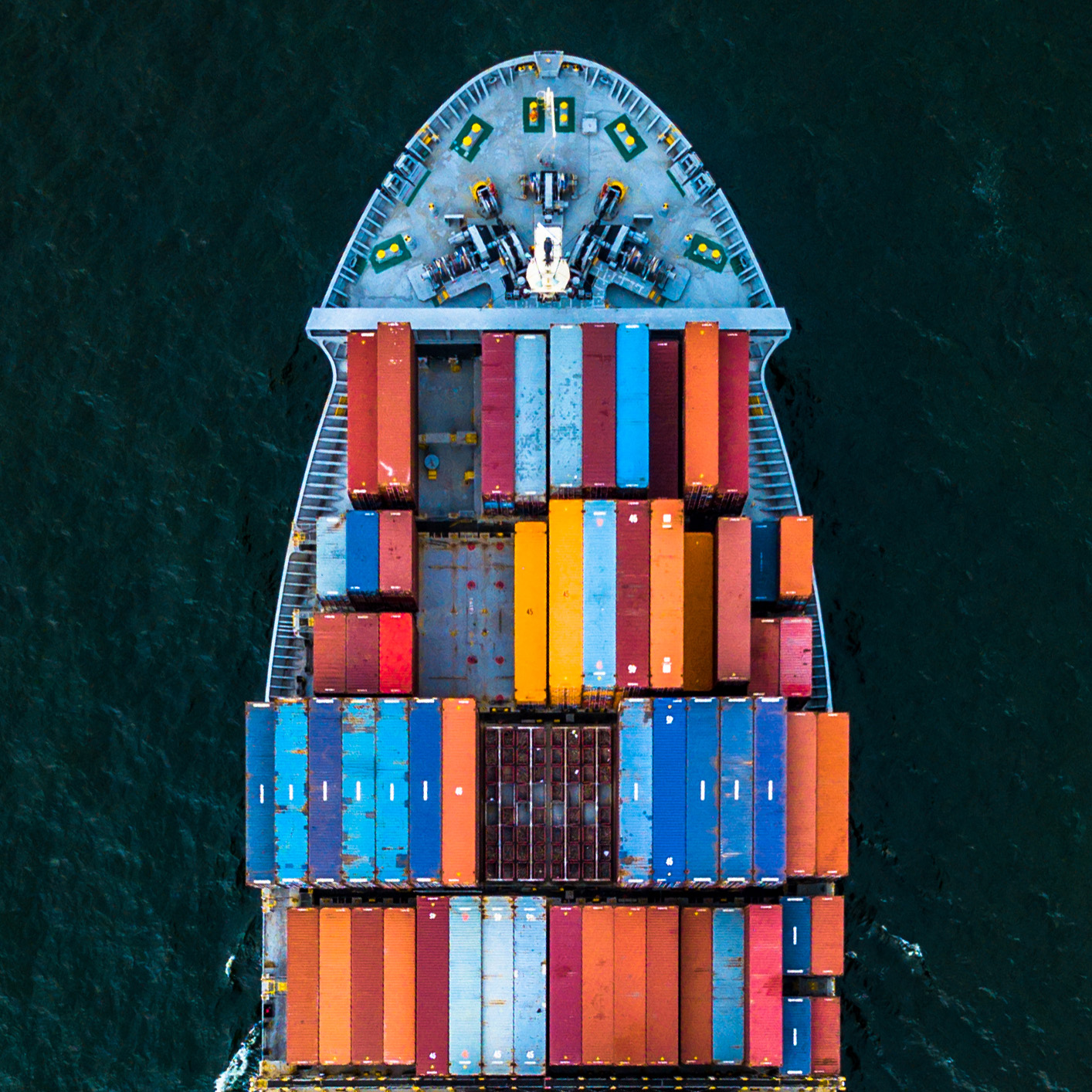 Aerial view of a cargo ship carrying multiple colorful shipping containers on dark blue water, symbolizing the global reach and logistics expertise of leading corporate law office teams and lawyers in Chicago.