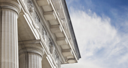 Close-up view of stone columns and ornate architectural details on a classical building, reflecting the distinguished presence of a corporate law office for lawyers in Chicago against a partly cloudy blue sky.