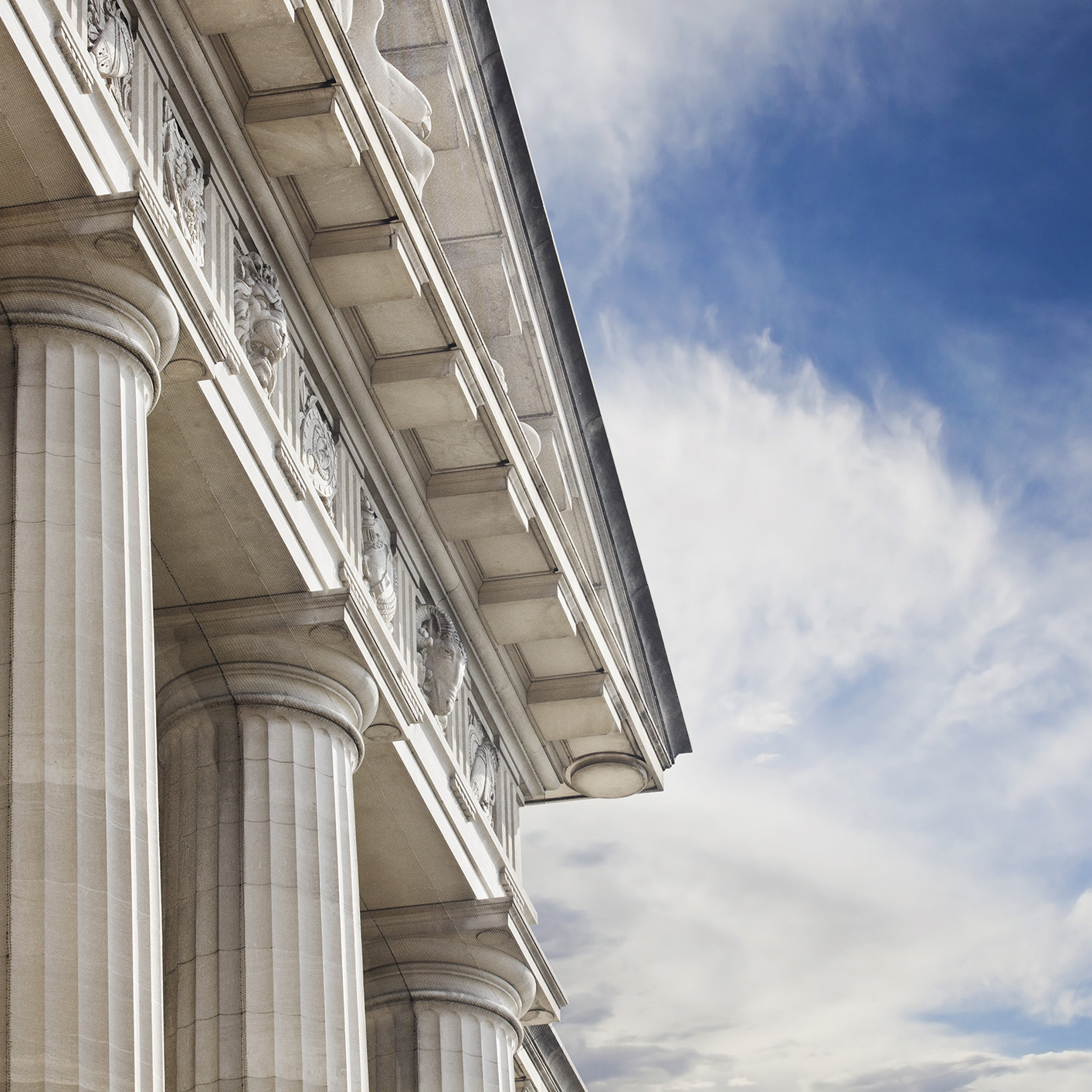 Close-up view of stone columns and ornate architectural details on a classical building, reflecting the distinguished presence of a corporate law office for lawyers in Chicago against a partly cloudy blue sky.