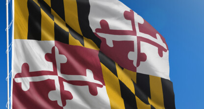 The Maryland state flag with black and gold checkers and red and white crosses flies against a clear blue sky, symbolizing heritage and pride—an inspiring sight outside any corporate law office.