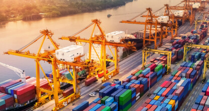 A busy port with large cranes loading shipping containers onto cargo ships at sunset, colorful containers lined up and a river in the background—much like the organized efficiency seen in top law offices or among leading lawyers in Chicago.