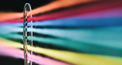 Close-up of multiple colorful threads passing through the eye of a sewing needle, intertwined like Chicago lawyers collaborating on complex cases, set against a dark background.