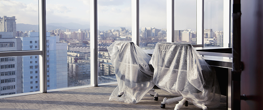 Two office chairs covered with plastic wrap sit next to a desk in a law office, in front of large windows overlooking a cityscape—an inspiring workspace for lawyers in Chicago.