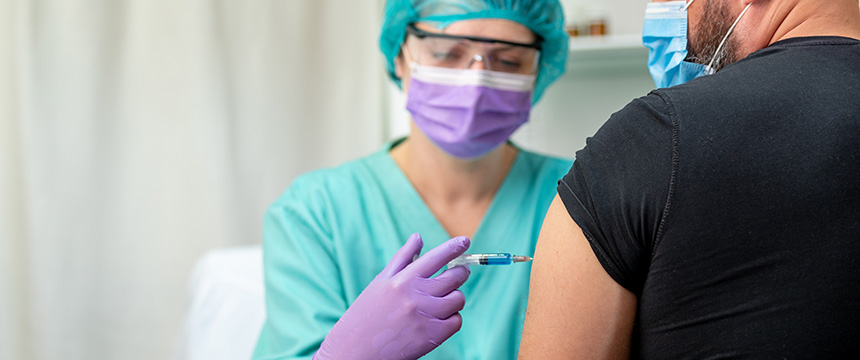 A healthcare worker wearing protective gear administers a vaccine to a person’s upper arm in a clinical setting, similar to how law offices provide litigation support with precision and care.