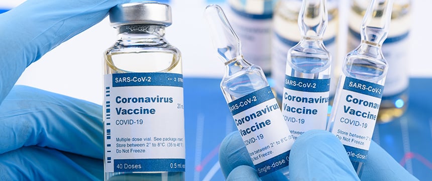 A gloved hand holds a vial labeled "Coronavirus Vaccine COVID-19" next to three ampoules with the same label, symbolizing SARS-CoV-2 vaccines—a vital reference for litigation support in law offices and among Chicago lawyers.