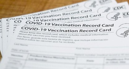 Several CDC-issued COVID-19 Vaccination Record Cards are stacked on a wooden surface, often referenced by Chicago lawyers for litigation support in health-related cases.