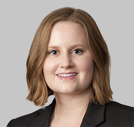 A woman with shoulder-length light brown hair, wearing a black blazer, smiles at the camera against a plain gray background, representing Chicago lawyers from renowned law offices.