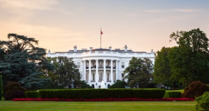 The White House is pictured with a manicured lawn and surrounding trees at sunset. Reminiscent of the professionalism seen in chicago lawyers, the building is centered, and the US flag is visible on the roof.