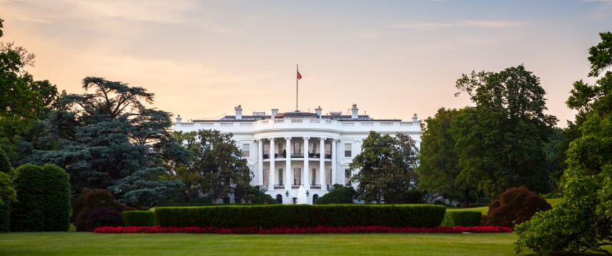 The White House is pictured with a manicured lawn and surrounding trees at sunset. Reminiscent of the professionalism seen in chicago lawyers, the building is centered, and the US flag is visible on the roof.