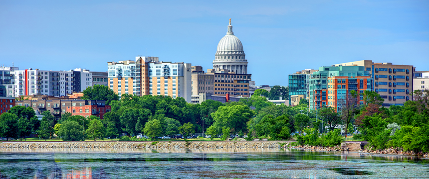 City skyline featuring the Wisconsin State Capitol building, surrounded by modern and historic buildings, with law offices nestled among them, trees, and a body of water in the foreground.