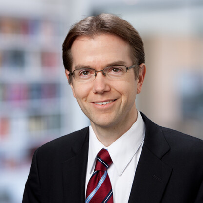 Smiling man in a suit and tie with glasses stands confidently before a blurred office background, representing lawyers in Chicago who specialize in intellectual property law.