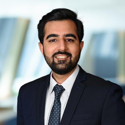 A man with dark hair and a beard, wearing a dark suit, white shirt, and patterned tie, smiles in a blurred office setting—an image representative of top Chicago lawyers.