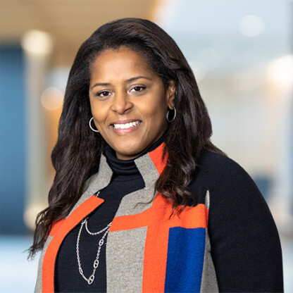 A woman with long dark hair wearing a black top and a geometric-patterned jacket stands indoors, smiling at the camera—reflecting the confidence often seen among Chicago lawyers specializing in intellectual property law.