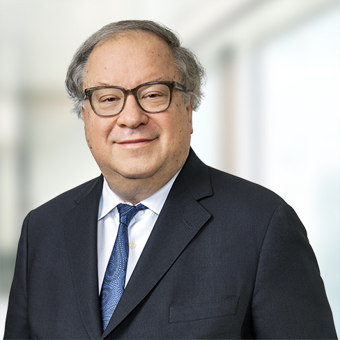 A middle-aged man with glasses and gray hair wearing a dark suit, blue patterned tie, and white shirt, stands in front of a blurred office background—reflecting the professionalism of lawyers in Chicago.