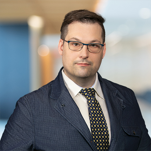 A man wearing glasses, a dark textured blazer, a white shirt, and a patterned tie stands in an office setting with a blurred background, reflecting the professional image of leading lawyers in Chicago.