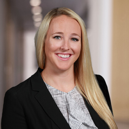 A woman with long blonde hair, wearing a black blazer and patterned blouse, smiles in a professional indoor setting at one of the top law offices offering litigation support for clients and lawyers in Chicago.