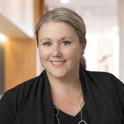 A woman with blonde hair pulled back, wearing a black top and jacket, smiles at the camera in a brightly lit indoor setting—reflecting the professionalism of lawyers in Chicago specializing in intellectual property law.