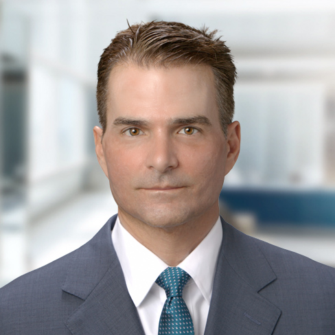 A man in a suit and tie poses for a professional headshot against a blurred office background, embodying the professionalism found at top law offices offering litigation support.