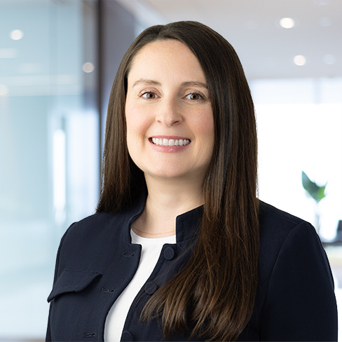 A woman with long brown hair, wearing a dark blazer over a white top, smiles at the camera in a modern corporate law office, reflecting the professionalism of lawyers in Chicago.