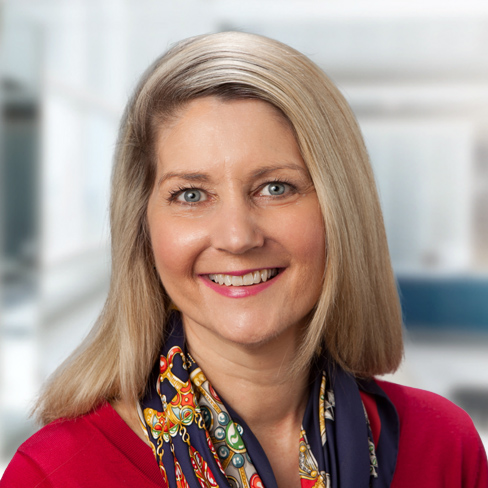A woman with straight blonde hair and a colorful scarf smiles at the camera in a brightly lit indoor setting, embodying the professionalism often seen among lawyers in Chicago.