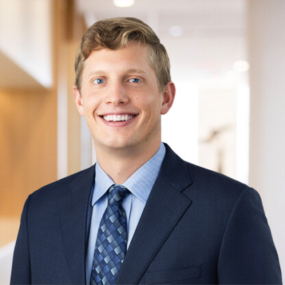 A man in a dark blue suit and patterned tie smiles at the camera, standing in a modern, well-lit office hallway—representing experienced lawyers in Chicago.