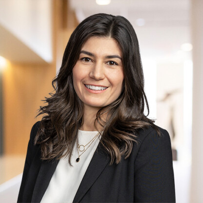 Woman with long dark hair wearing a black blazer and white top, smiling, stands in a modern corporate law office hallway—an inviting presence among Chicago lawyers and litigation support professionals.
