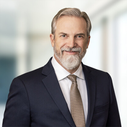 A middle-aged man with gray hair and beard, wearing a dark suit, white shirt, and patterned tie, stands in front of a blurred corporate law office—a confident professional among top lawyers in Chicago.