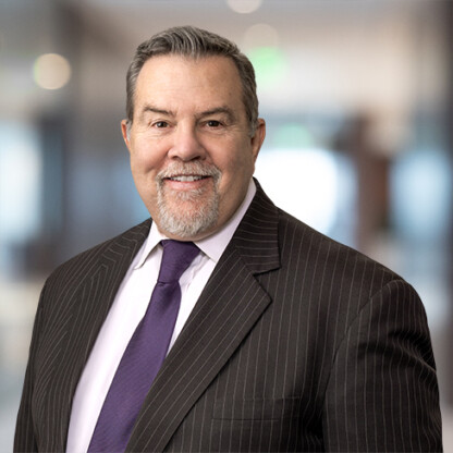 Middle-aged man with gray hair and goatee wearing a pinstripe suit, white shirt, and purple tie, standing in a blurred corporate law office, representing Chicago lawyers specializing in litigation support.