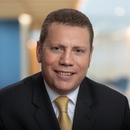 A man in a dark pinstripe suit, light shirt, and yellow tie is smiling at the camera in a corporate law office, with a blurred background typical of top Chicago lawyers.