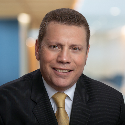 A man in a dark pinstripe suit, light shirt, and yellow tie is smiling at the camera in a corporate law office, with a blurred background typical of top Chicago lawyers.