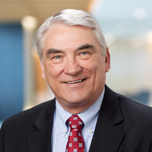 Smiling older man with gray hair in a dark suit, white shirt, and patterned red tie, posed in an office setting with a blurred background—ideal for law offices or litigation support teams seeking experienced lawyers in Chicago.
