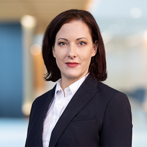 A woman with straight, shoulder-length brown hair wearing a white shirt and dark blazer stands in a modern, blurred office setting, representing the professionalism of top lawyers in Chicago.