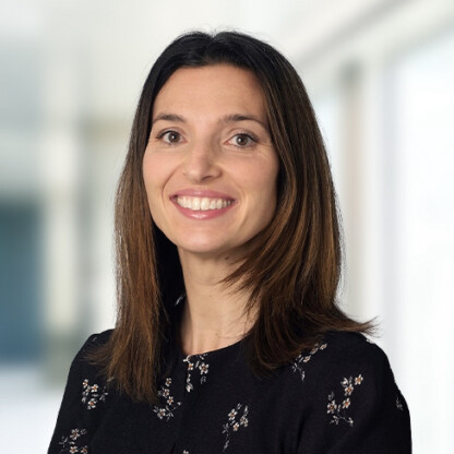 A woman with straight brown hair, wearing a black floral top, smiles at the camera in a brightly lit corporate law office with a blurred background, reflecting the welcoming atmosphere of chicago lawyers.