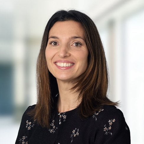 A woman with straight brown hair, wearing a black floral top, smiles at the camera in a brightly lit corporate law office with a blurred background, reflecting the welcoming atmosphere of chicago lawyers.