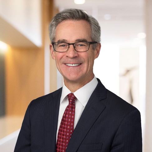 A middle-aged man in a suit, red tie, and glasses stands smiling in a brightly lit corporate law office hallway, reflecting the professionalism of top Chicago lawyers.